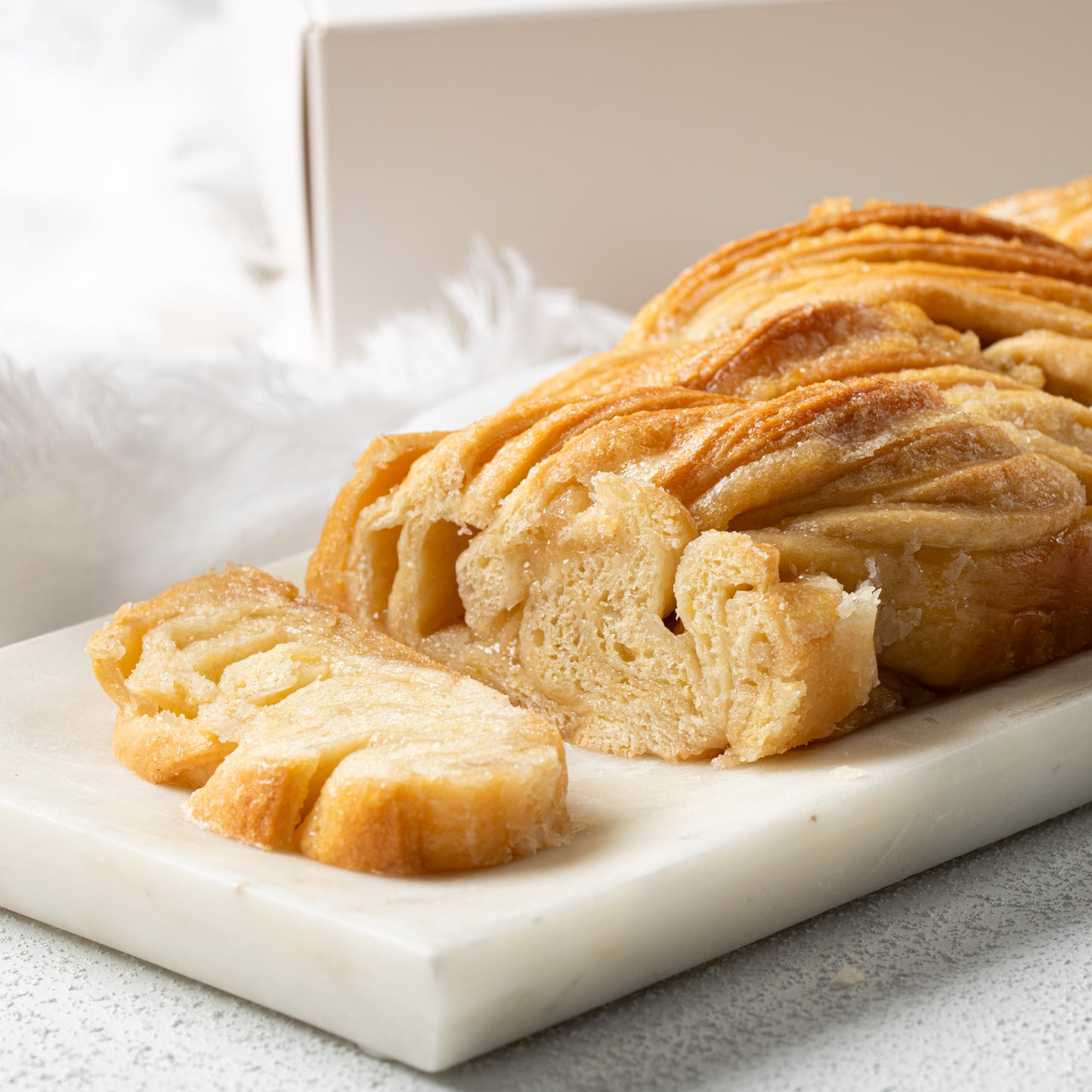 A close-up of Babkatoure’s Vanilla Babka, showcasing its sliced, golden-brown layers and delicious vanilla filling, served on a white marble cutting board.